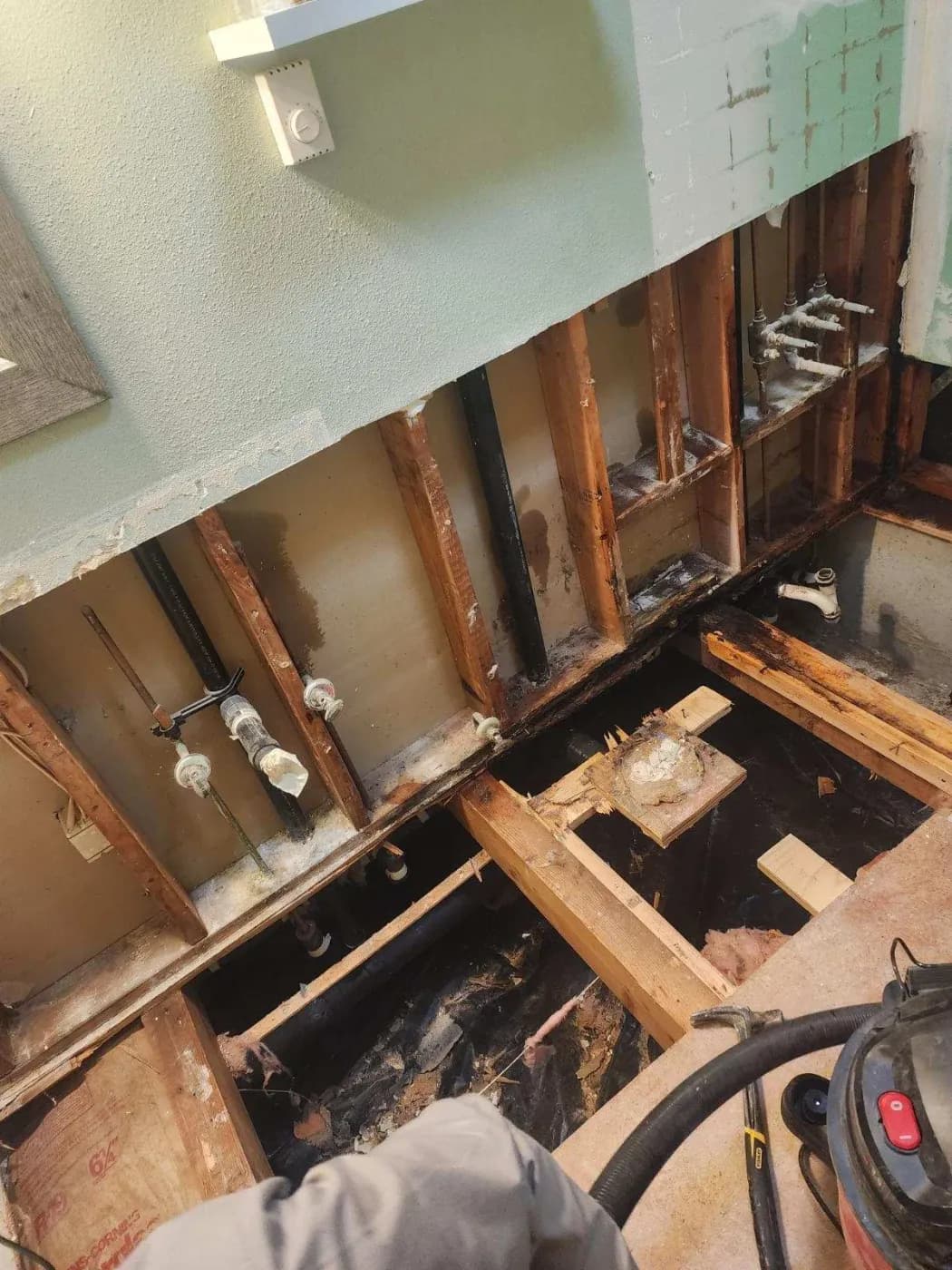 Water-damaged wall cavity with exposed wood framing, wet insulation and plumbing lines opened up for mitigation